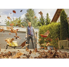 Mann benutzt einen Laubbläser, um Blätter auf einem Hof zu entfernen.