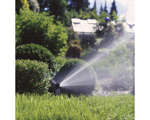 Versenkregner bewässert einen grünen Rasen in einem Garten.