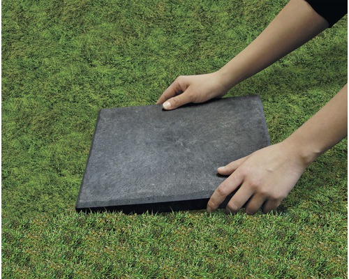 Person verlegt eine Gehwegplatte im Garten.