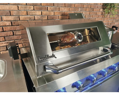 Buschbeck Grill mit Brathähnchen auf dem Grillspieß vor einer Backsteinmauer