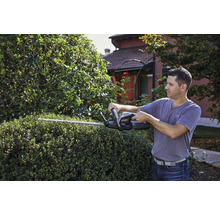 Ein Mann schneidet eine Hecke mit einer Heckenschere im Garten.