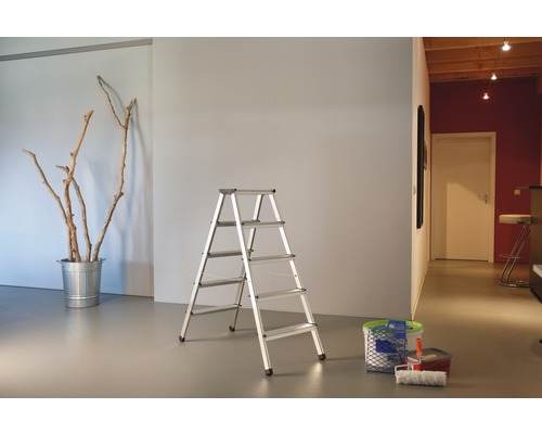 Raumansicht mit einer Aluminium-Stufenleiter, einem Eimer mit Zweigen und Malutensilien