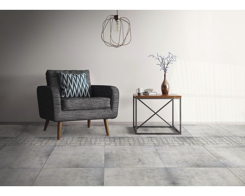 Wohnzimmer mit grauem Sessel, Holztisch, Lampe und Bodenfliesen.