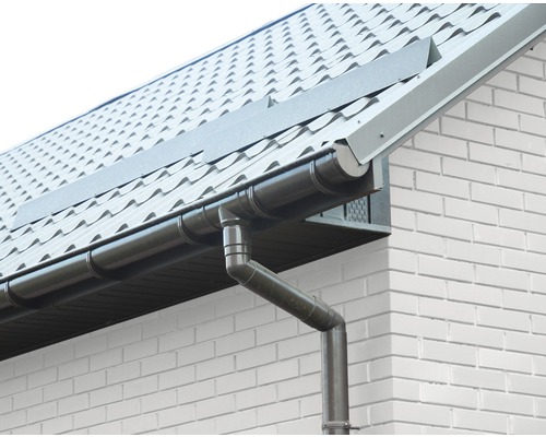 Dachrinne und Fallrohr an einem Haus mit Ziegeldach und weißer Backsteinfassade.