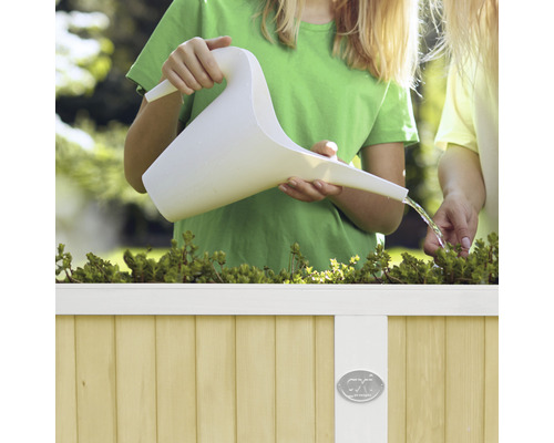 Kind gießt Pflanzen mit einer Gießkanne in einem Hochbeet.