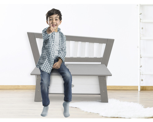 Junge sitzt auf einer grauen Spielzeugtruhenbank im Kinderzimmer
