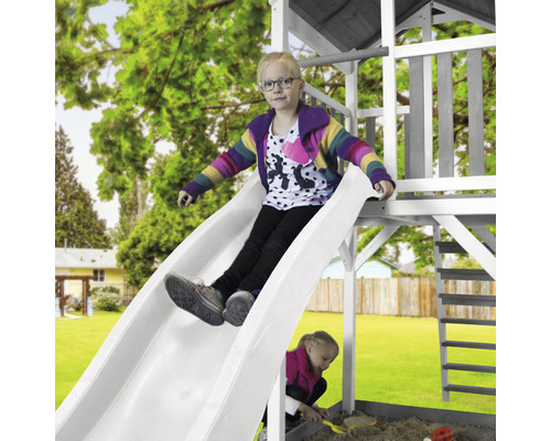Mädchen rutscht auf einer weißen Rutsche eines Spielturms im Garten.