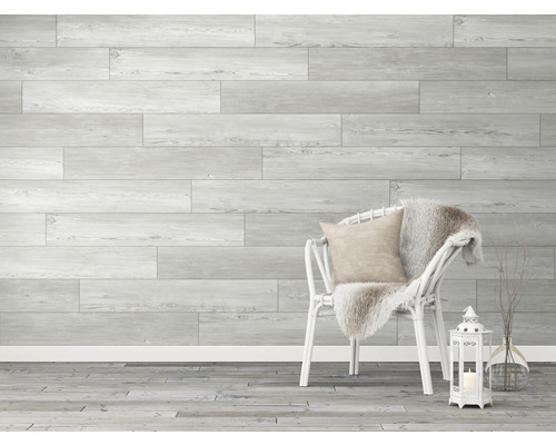 Wandpaneele in Holzoptik, weißer Stuhl mit Kissen und Decke, Laterne und Vase mit Zweigen in einem hellen Raum.