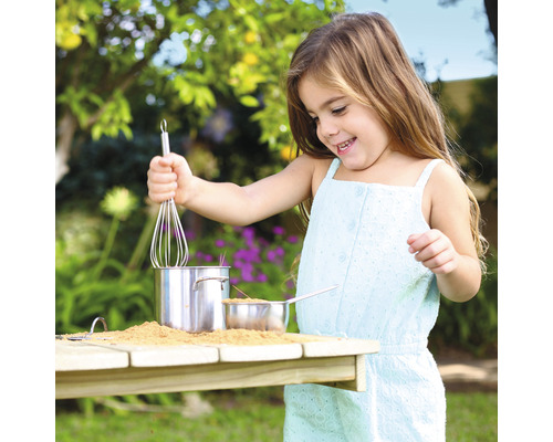 Mädchen spielt mit Töpfen, Sand und Schneebesen im Garten