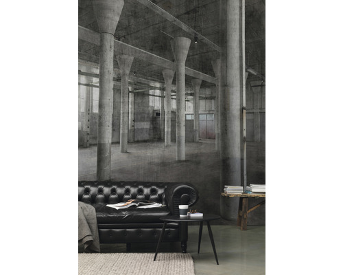Wohnraum mit schwarzem Ledersofa vor einer Fototapete mit einem Fabrikhallenmotiv