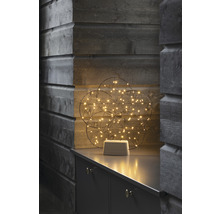 Dekorative Leuchtkugel mit LED-Lichtern auf einem grauen Möbelstück vor einer Holzwand.