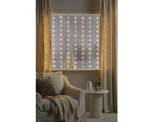 Dekoratives Wohnzimmer mit Sternenlichterkette vor dem Fenster, Sessel und Beistelltisch