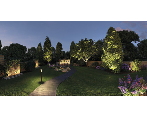 Beleuchteter Garten mit Weg, Bäumen, Büschen und Blumen bei Dämmerung.