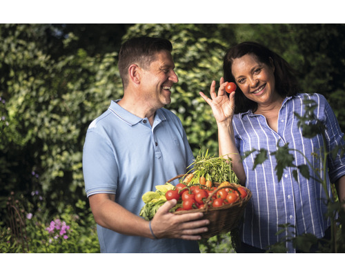 Lächelndes Paar mit geerntetem Gemüse im Garten