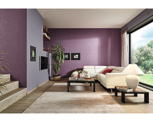 Wohnzimmer mit Sofa, Tisch, Teppich und Zimmerpflanzen vor einer gemusterten Wand