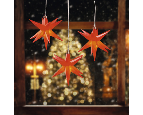 3er-Set LED Sternenhänger Ø 12 cm 3 LEDs Lichtfarbe warmweiß rot Drei rote Sterne als Fensterdekoration vor verschneiter Landschaft und Weihnachtsbaum