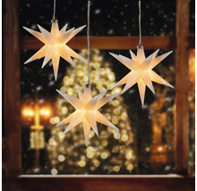 Drei leuchtende Sterne als Dekoration vor einem Fenster zur Weihnachtszeit.