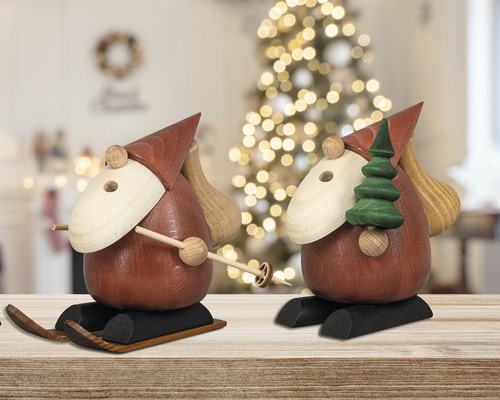 Zwei Räuchermännchen aus Holz auf Skiern mit Weihnachtsbaum und Sack im Hintergrund
