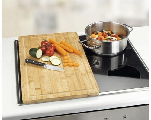 Bambus Schneidebrett auf einem Herd mit Gemüse und einem Topf