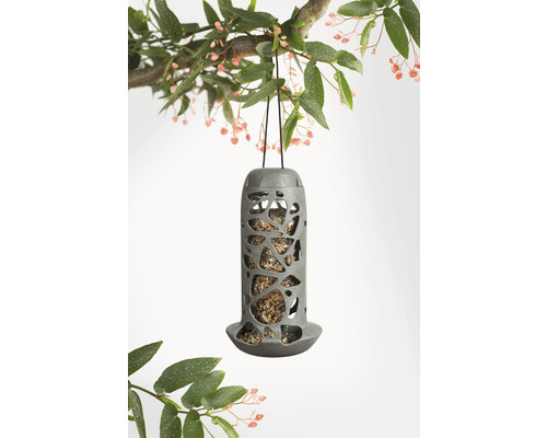 Grauer Vogelfutterspender hängt an einem Ast mit Blättern und Blüten.