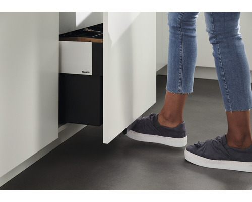 Frau öffnet einen Küchenschrank mit einer Fußbedienung. Im Schrank befindet sich ein Mülleimer von Blanco.