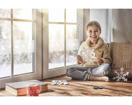 Mädchen sitzt am Fenster und bastelt Schneeflocken
