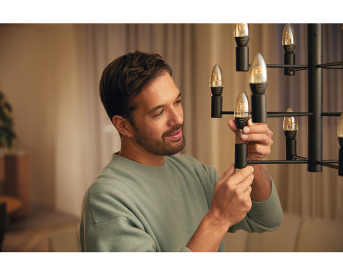 Mann wechselt eine LED Lampe in einem Leuchter aus