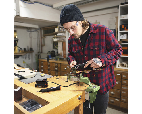 Mann mit Schutzbrille bearbeitet Metall mit einem Winkelschleifer in einer Werkstatt.