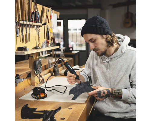 Mann arbeitet mit einem Multifunktionswerkzeug an einem Werkstück in einer Werkstatt.