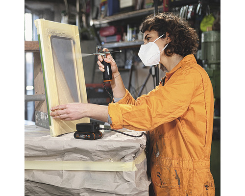 Frau verwendet eine Farbspritzpistole zum Malen eines Fensterrahmens