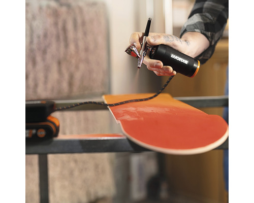 Eine Person benutzt eine Airbrushpistole von Worx, um ein Holzbrett zu bemalen.