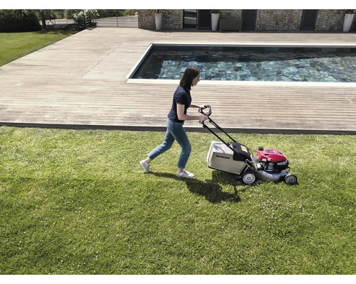 Eine Frau mäht mit einem Rasenmäher von Honda den Rasen in einem Garten mit Pool.