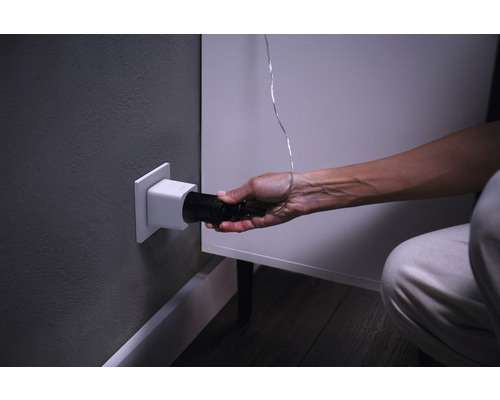Eine Person steckt einen schwarzen Stecker in eine weiße Steckdose in der Wand.