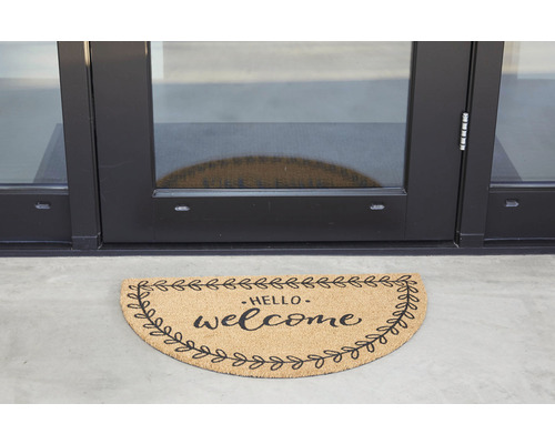 Halbrunde Fußmatte mit der Aufschrift ''Hello welcome'' vor einer Tür.