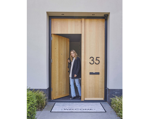 Eine einladende Haustür mit Hausnummer, Briefkasten und Fußmatte mit Willkommensgruß