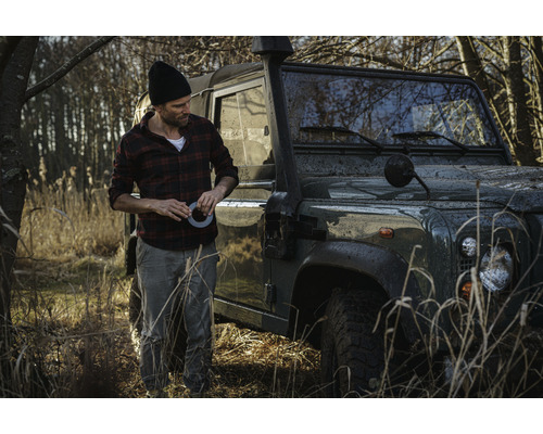 Mann mit Klebeband neben einem Geländewagen im Gelände.