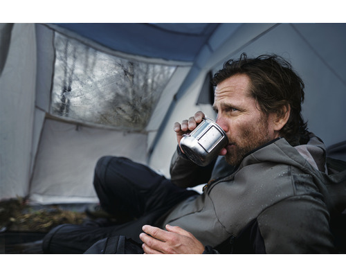 Mann trinkt aus einer Tasse in einem Zelt