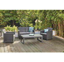Gartensitzgruppe mit Sofa, Sessel und Tisch auf einer Holzterrasse vor Büschen