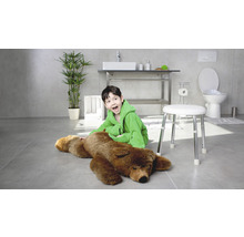 Helles Badezimmer mit einem Jungen im Bademantel, der neben einem Bären auf einem Hocker sitzt, mit Waschbecken, Toilette und Pflanze