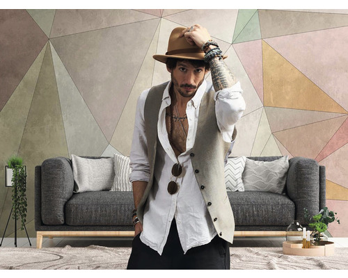Wohnzimmer mit geometrischer Tapete, grauer Couch und einem Mann mit Hut