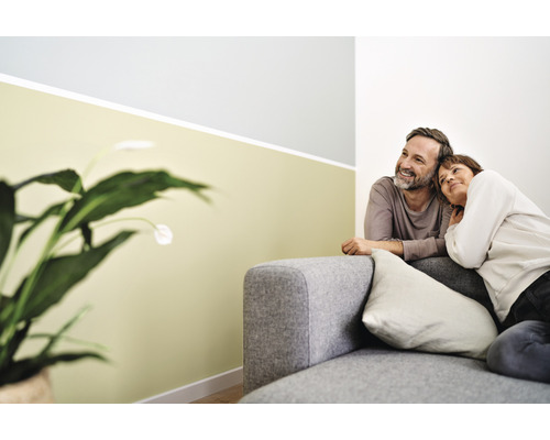 Ein Paar entspannt auf einem grauen Sofa in einem hellen Wohnzimmer mit Zimmerpflanze.