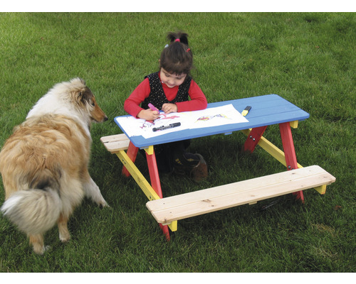 Kind sitzt am Kindertisch mit Hund im Garten und malt
