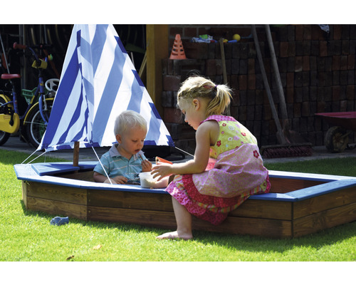 Zwei Kinder spielen in einem Sandkasten in Schiffsform mit Segel.