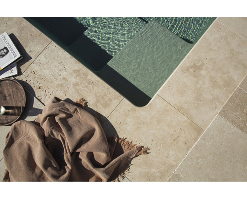 Detailansicht eines Pools mit Natursteinfliesen, einem Buch, einem Getränk und einem Tuch