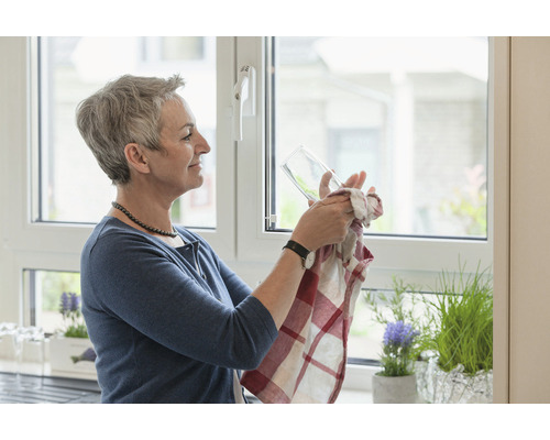 Frau trocknet Glas mit Küchentuch in heller Küche