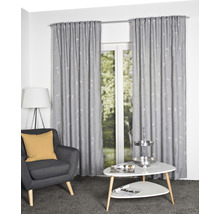 Wohnzimmer mit grauem Sessel, weißem Tisch und grauen Gardinen mit Muster vor einem Fenster