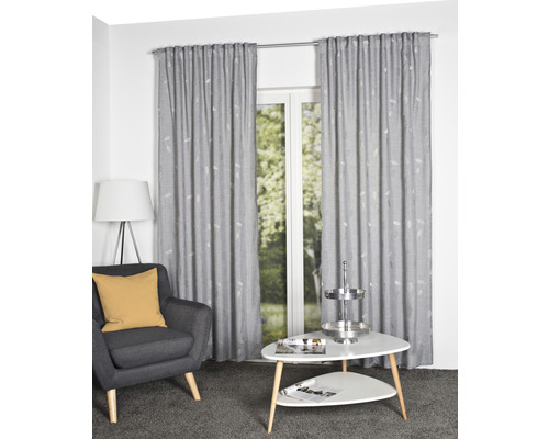 Wohnzimmer mit grauem Sessel, weißem Tisch und grauen Gardinen mit Muster vor einem Fenster