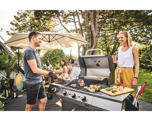 Grillszene mit Mann und Frau an einem Gasgrill im Garten mit Gästen