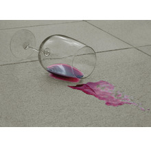 Umgekipptes Weinglas mit ausgelaufenem Wein auf Fliesen