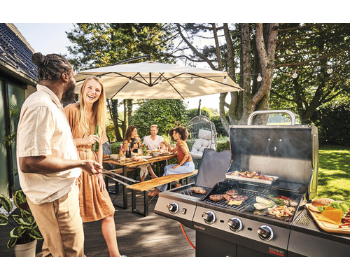 Personen grillen im Garten mit einem Gasgrill unter einem Sonnenschirm und einer Lichterkette.